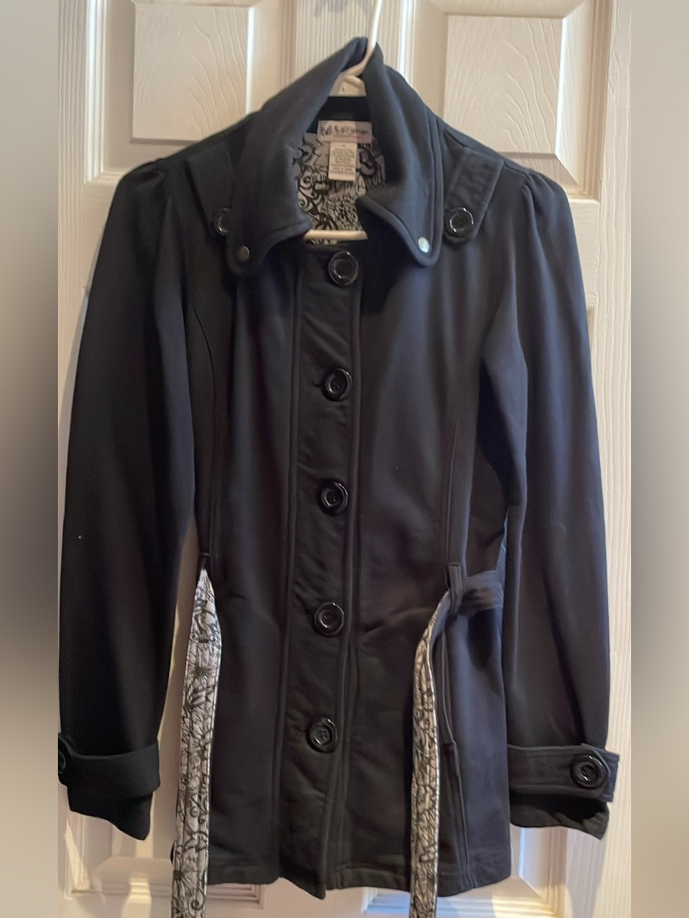 Stylish black coat. Has button-front closure and collar. Belt has patterned unde